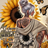 Woman with tattoos and sunflowers on hoodie, in front of large sunflower and butterflies.
