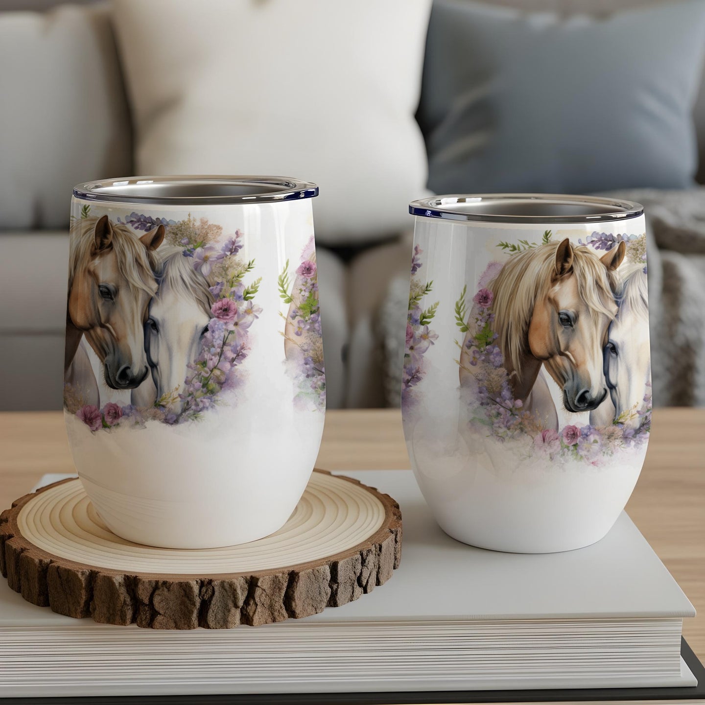 Two wine tumblers with horses and floral designs, on a wooden coaster.