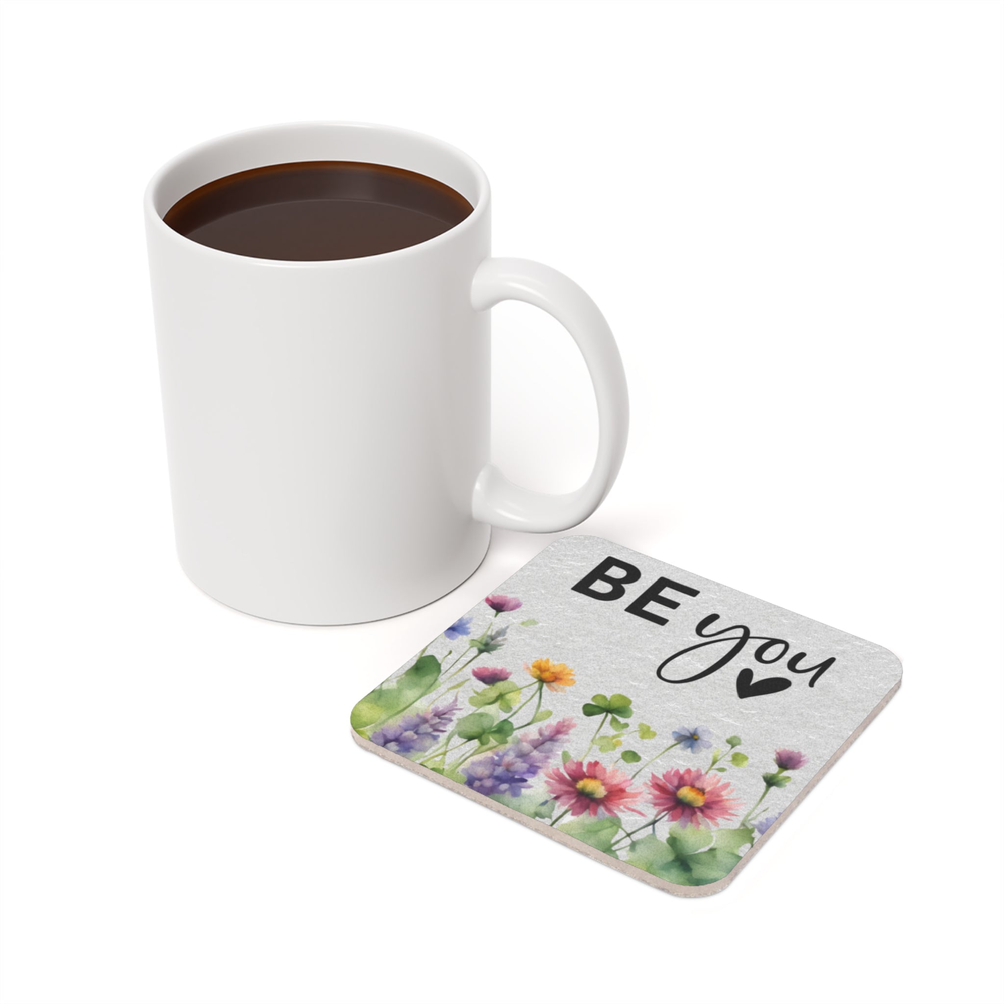 White mug of coffee next to a coaster with "BE YOU" and watercolor flowers.