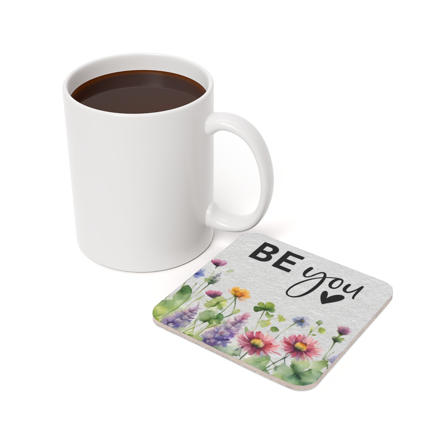 White mug of coffee next to a coaster with "BE YOU" and watercolor flowers.