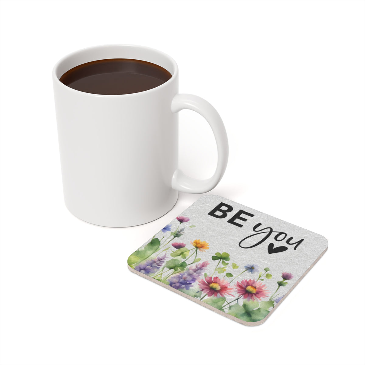 White mug of coffee next to a coaster with "BE YOU" and watercolor flowers.