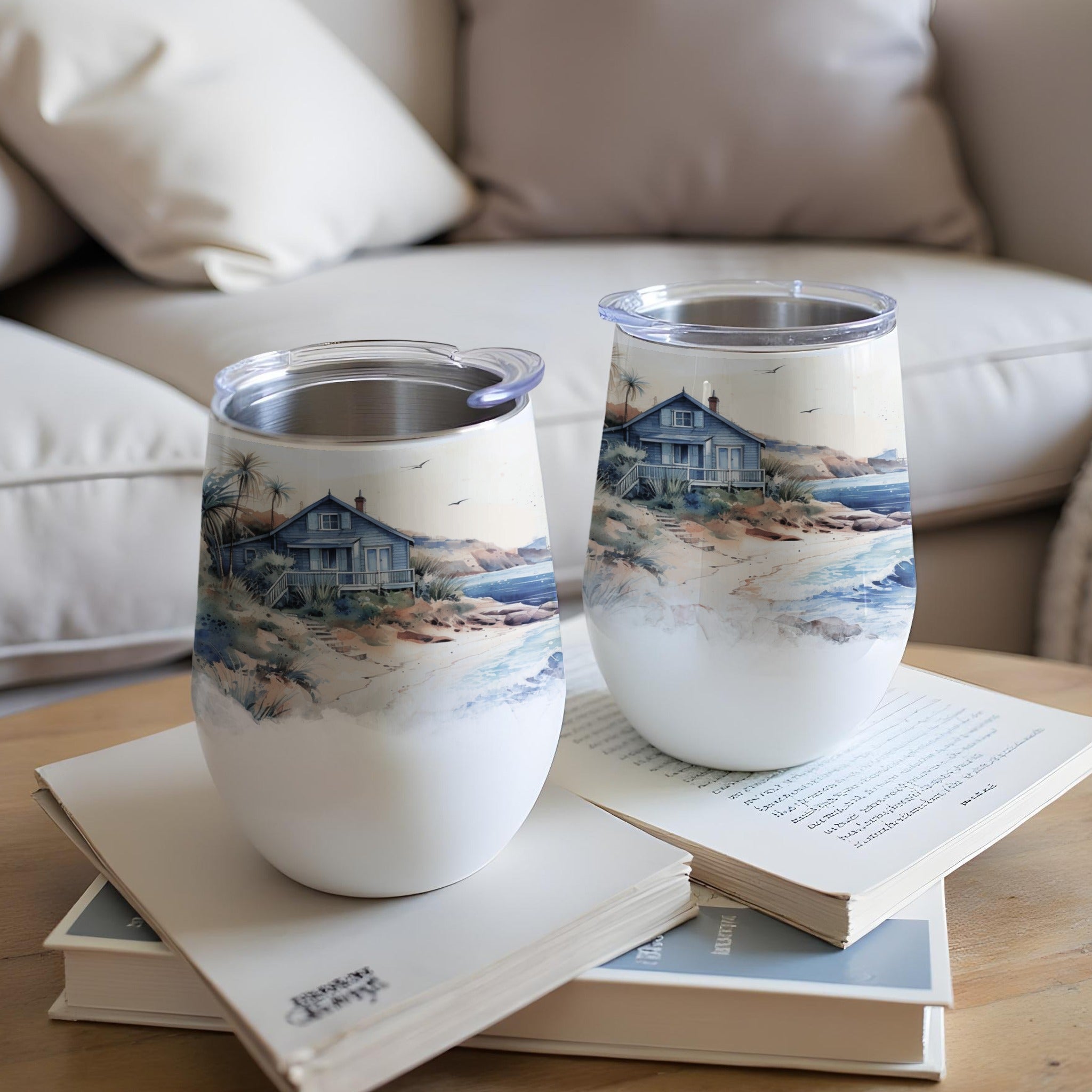 Two tumblers with a beach house watercolor design rest on books.
