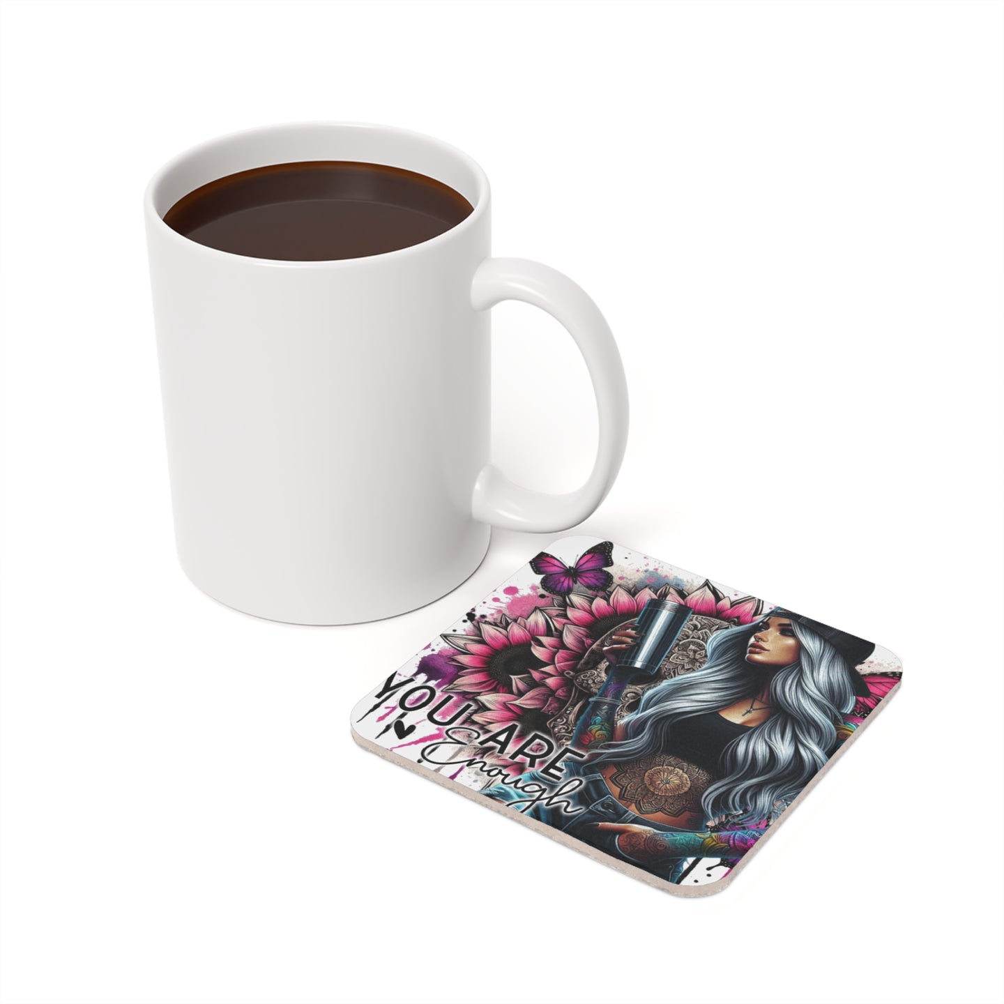 White mug with coffee beside a coaster featuring a woman and sunflowers.