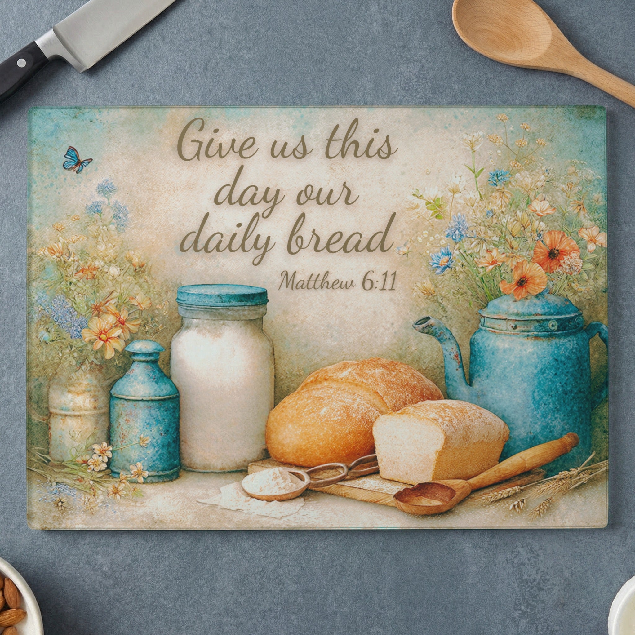 Glass cutting board with bread, blue teapot, jars, and Matthew 6:11 quote.