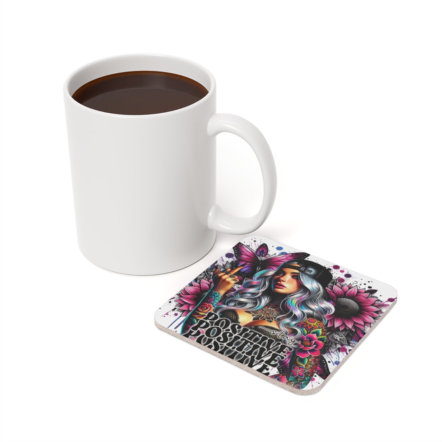 White mug of coffee next to a coaster with a colorful tattoo-style design.