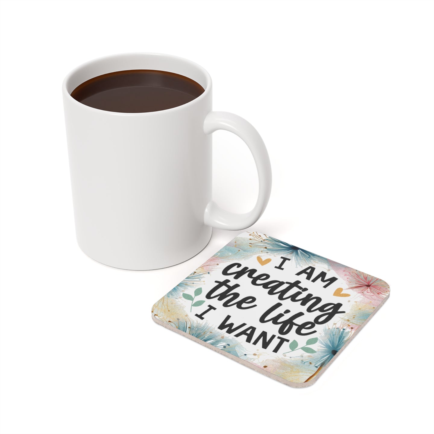 White mug of coffee next to a coaster with "I AM creating the life I WANT" text.