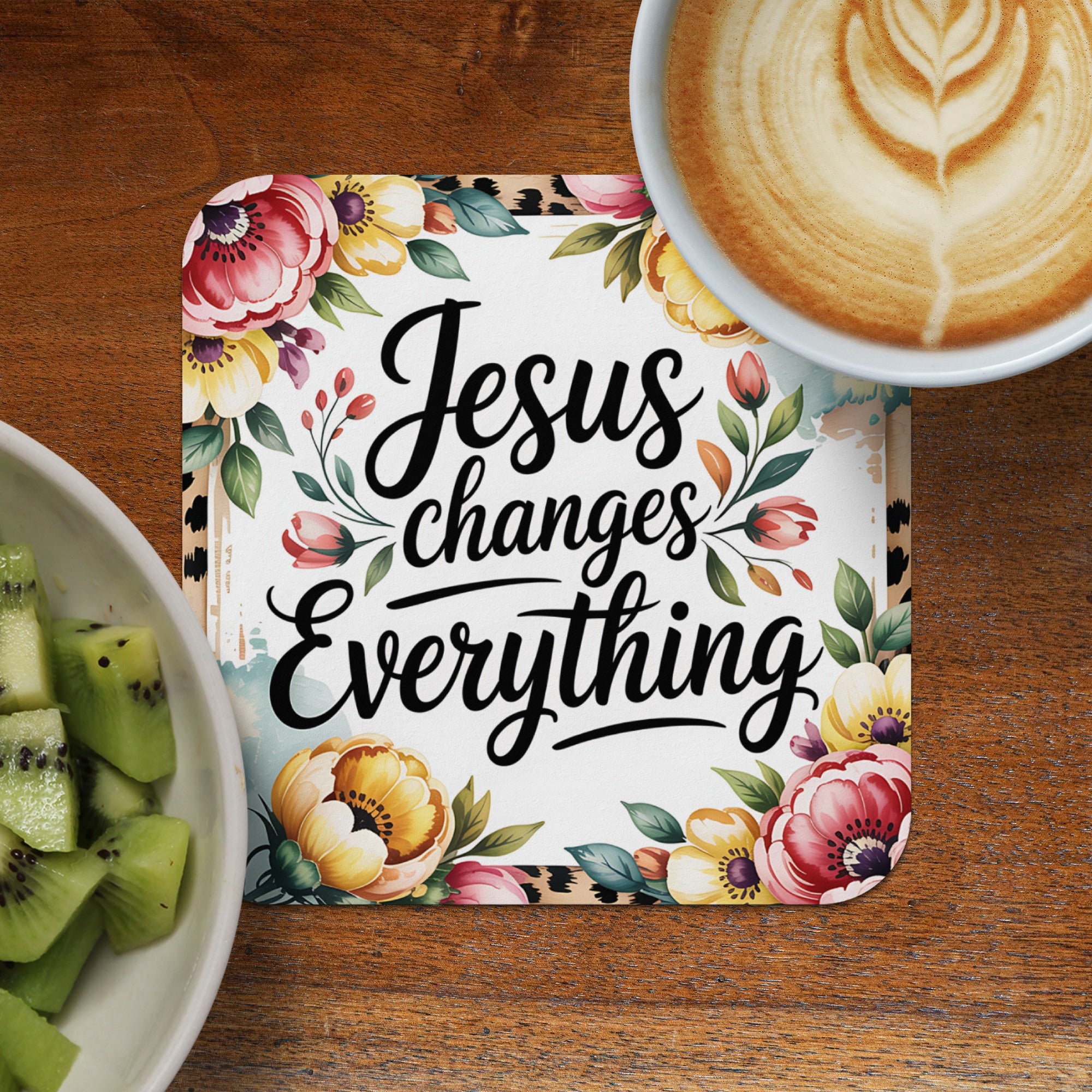 Coaster with "Jesus changes everything" in script over floral design, beside kiwi and coffee.