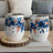 Two white wine tumblers with blue floral and feather design.