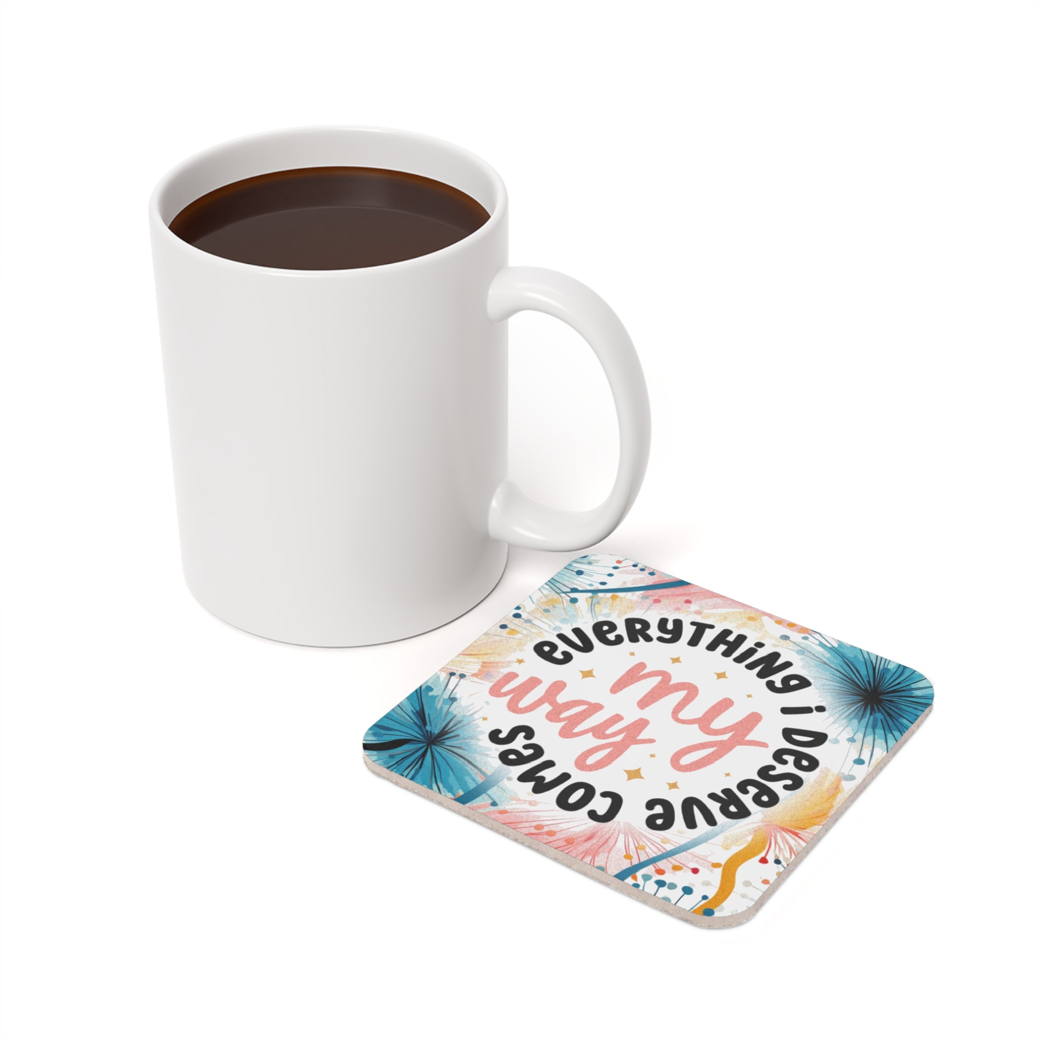White mug with coffee next to a round coaster with floral design and text.