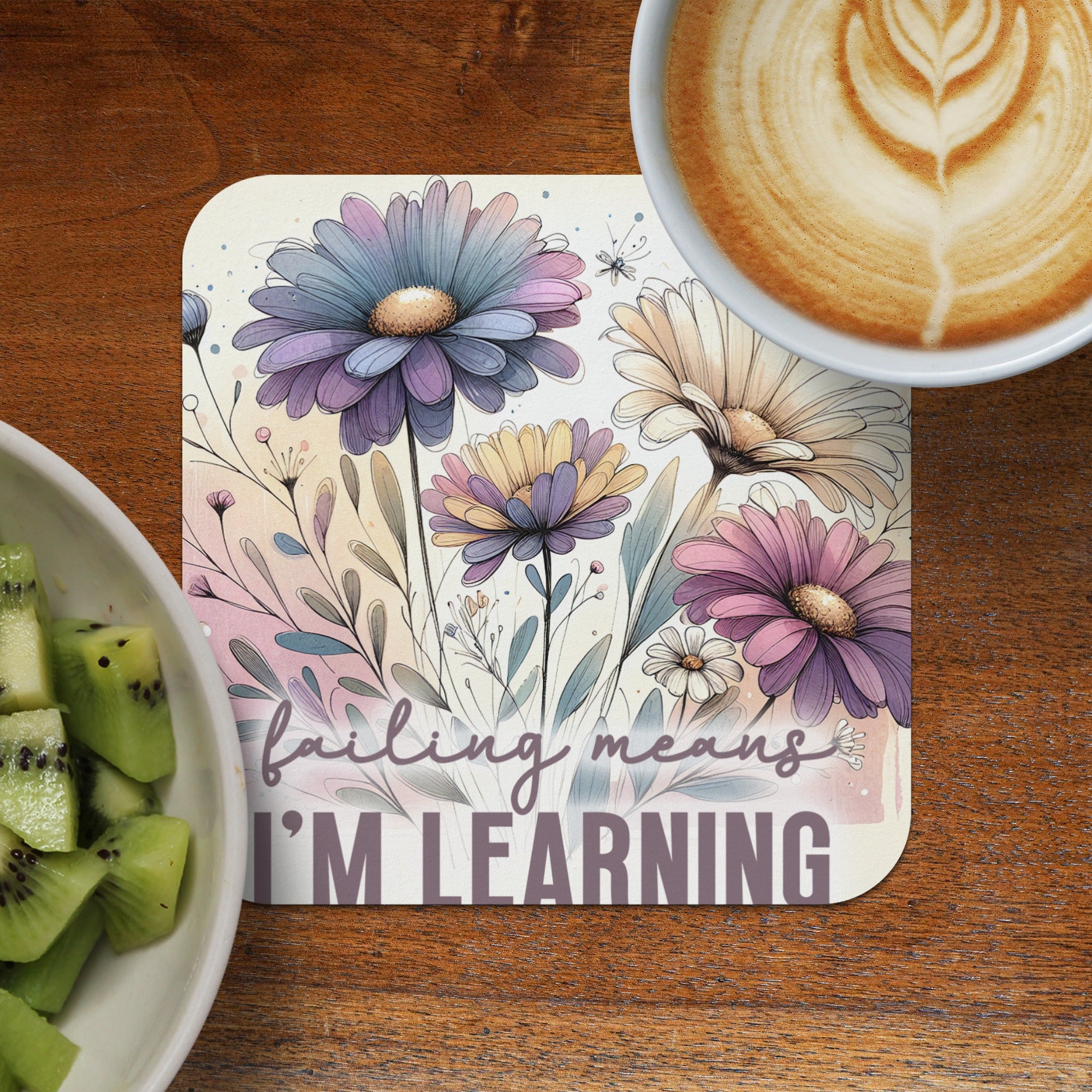 Floral coaster with "failing means I'M LEARNING" text, next to kiwi slices and coffee.