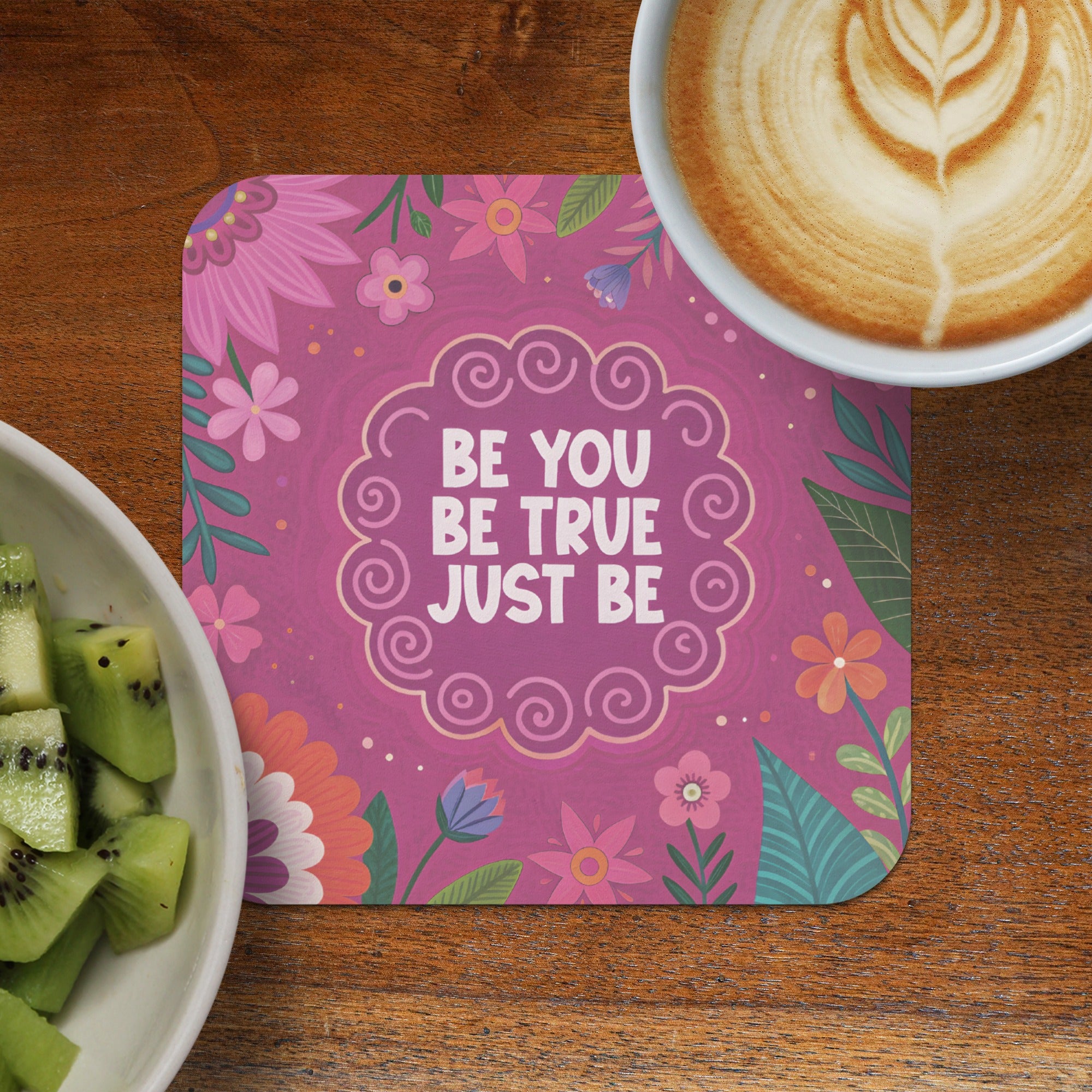 Pink floral coaster with "Be You. Be True. Just Be." text next to coffee and kiwi.