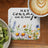 Coaster with floral design and "Have courage and be kind" text next to coffee and kiwi.