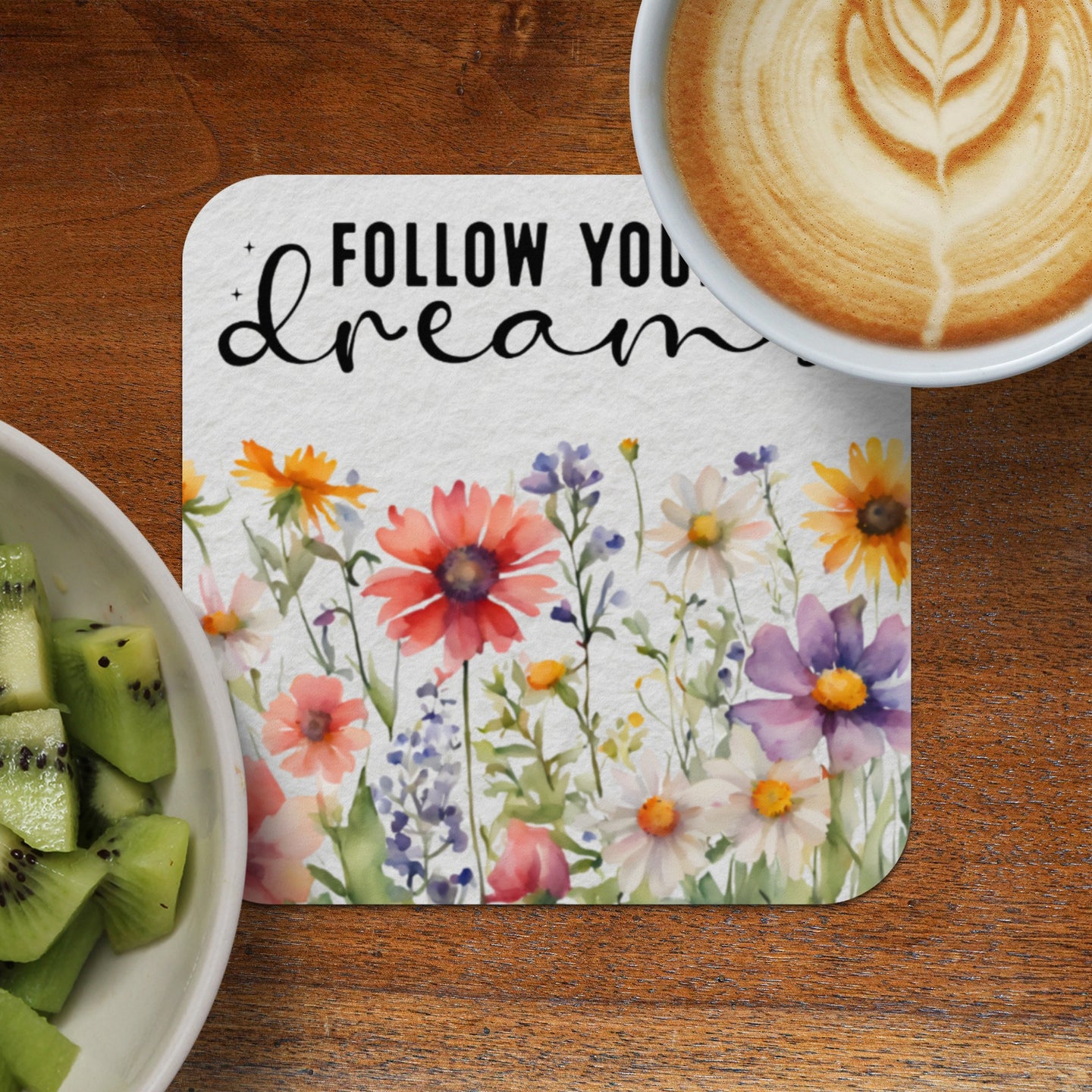 Floral watercolor coaster with "Follow your dreams" text next to kiwi slices and coffee.