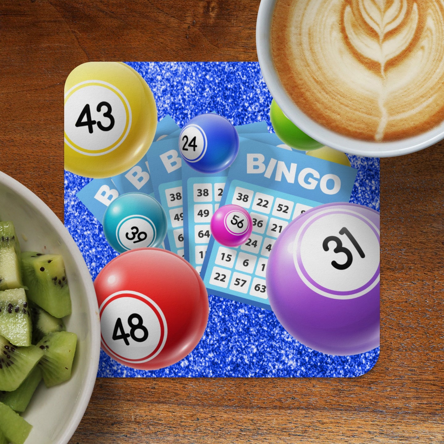 Bingo cards with numbers, colorful bingo balls, sliced kiwi, and coffee on a wooden table.