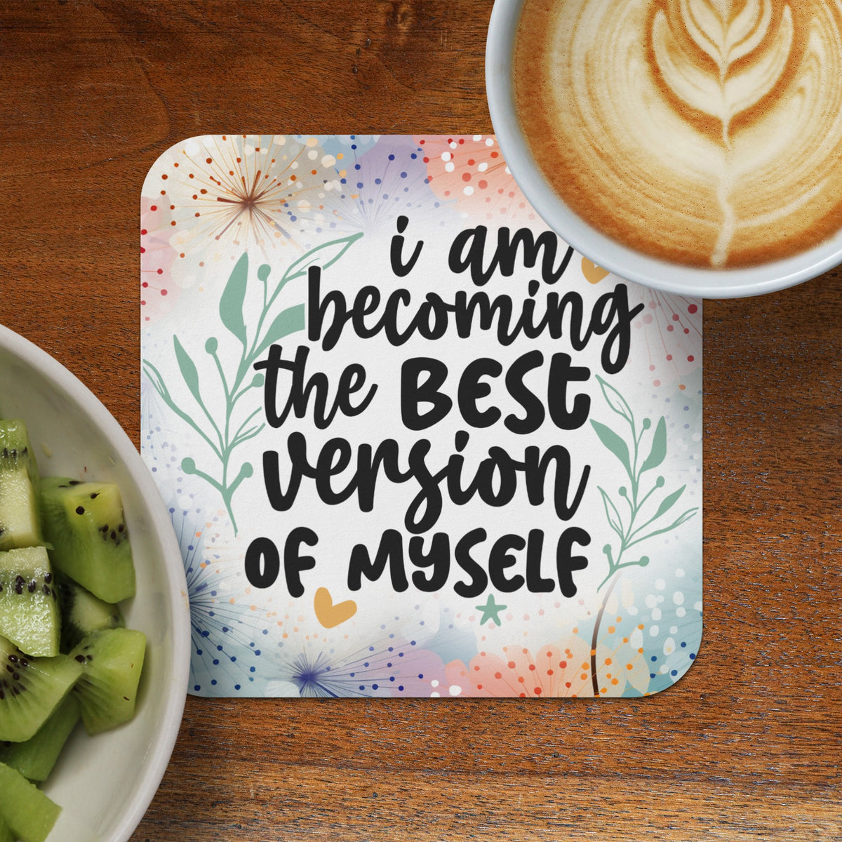 Coaster with "I am becoming the BEST version of myself" text next to kiwi slices and coffee.