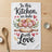 Kitchen towel with watercolor cookies and text "In this Kitchen, we bake with Love."