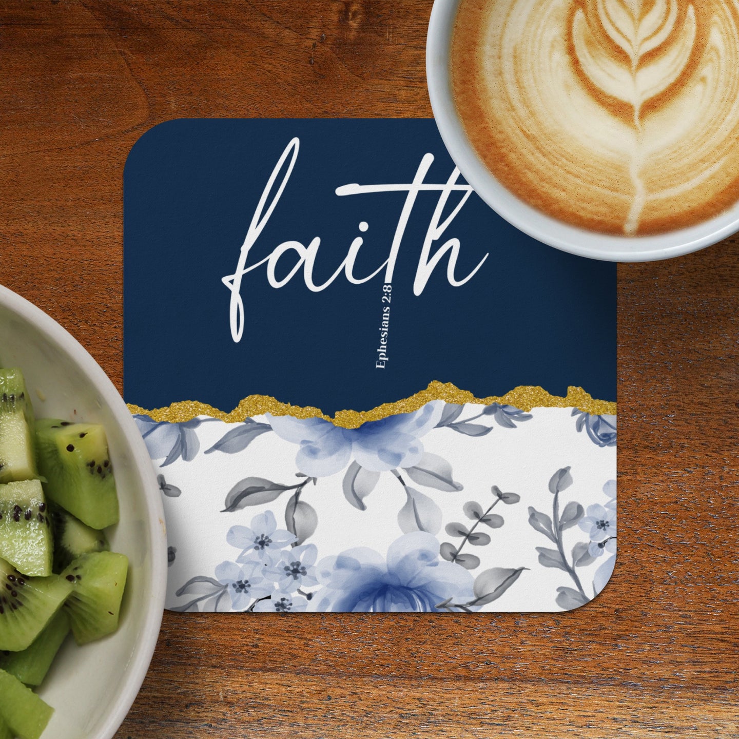 Dark blue coaster with "faith" and floral pattern next to fruit and coffee.