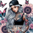 Woman with tattoos and long gray hair, wearing a black baseball cap, with sunflowers and butterflies.