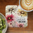 Coaster with daisy flowers and "Believe Believe" text next to kiwi slices and coffee.
