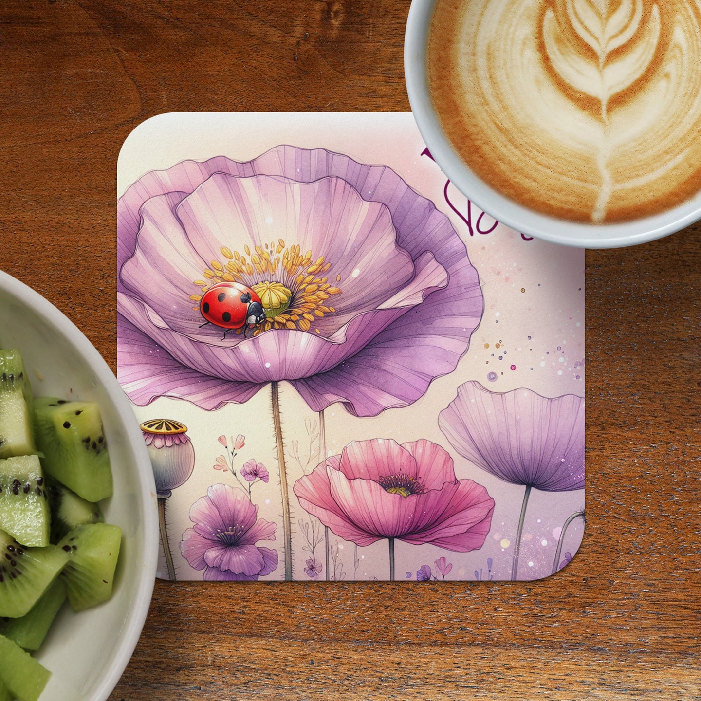 Round coaster with purple poppies and ladybug, beside kiwi slices and coffee.