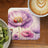 Round coaster with purple poppies and ladybug, beside kiwi slices and coffee.