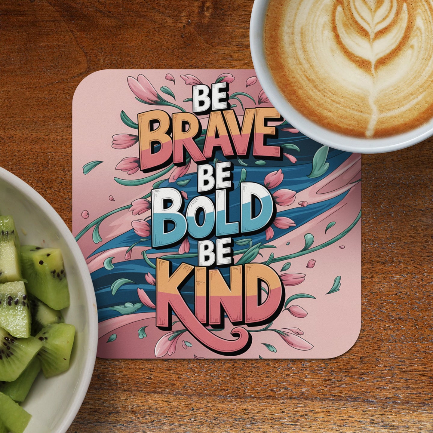 Coaster with "Be Brave, Be Bold, Be Kind" text and floral design, next to kiwi slices and coffee.