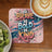 Coaster with "Be Brave, Be Bold, Be Kind" text and floral design, next to kiwi slices and coffee.