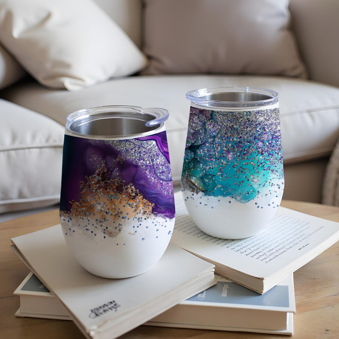 Two tumblers with swirling purple and blue glitter designs sit on open books.