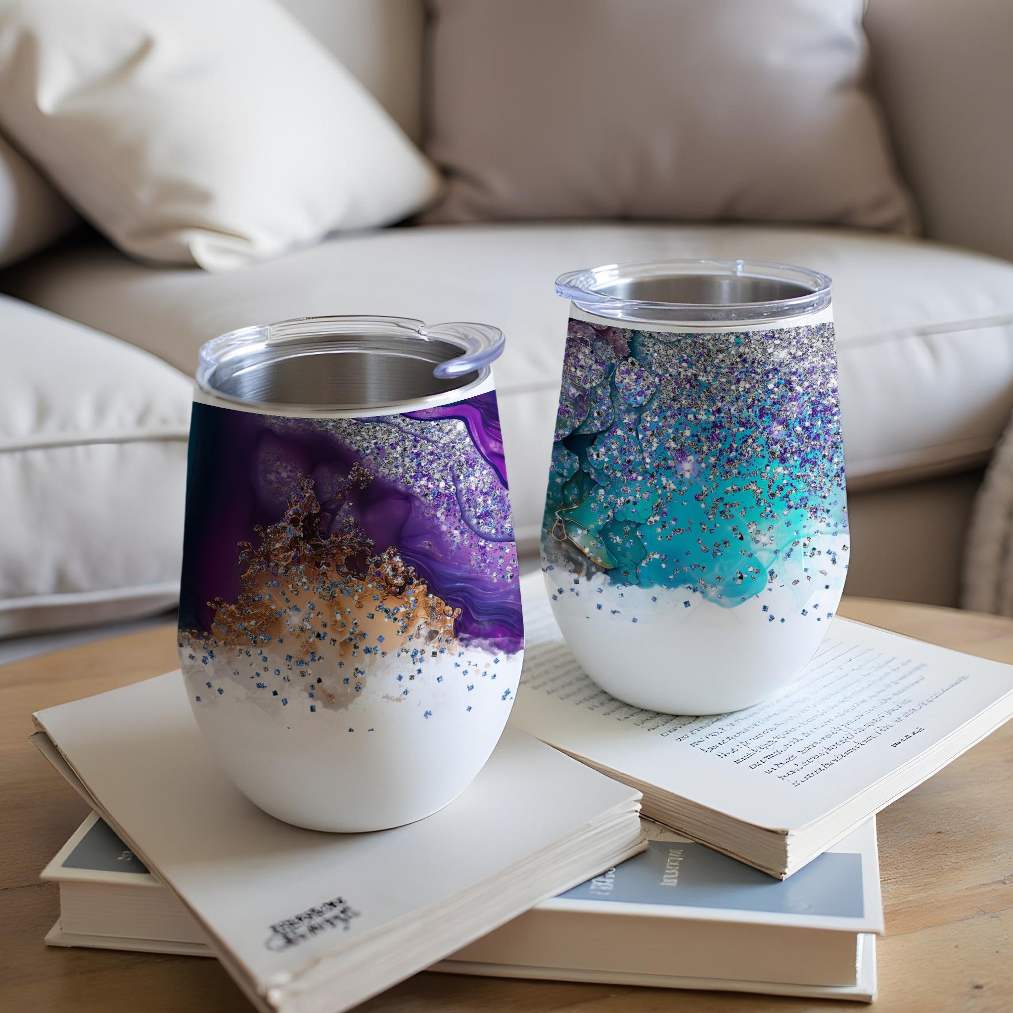 Two tumblers with swirling purple and blue glitter designs sit on open books.