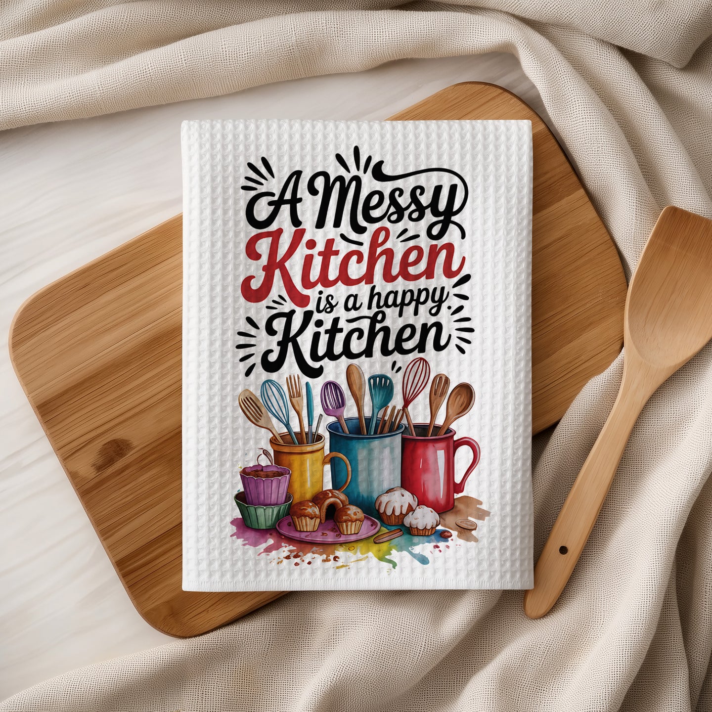 White waffle weave kitchen towel with "A Messy Kitchen is a Happy Kitchen" text and kitchen utensils.