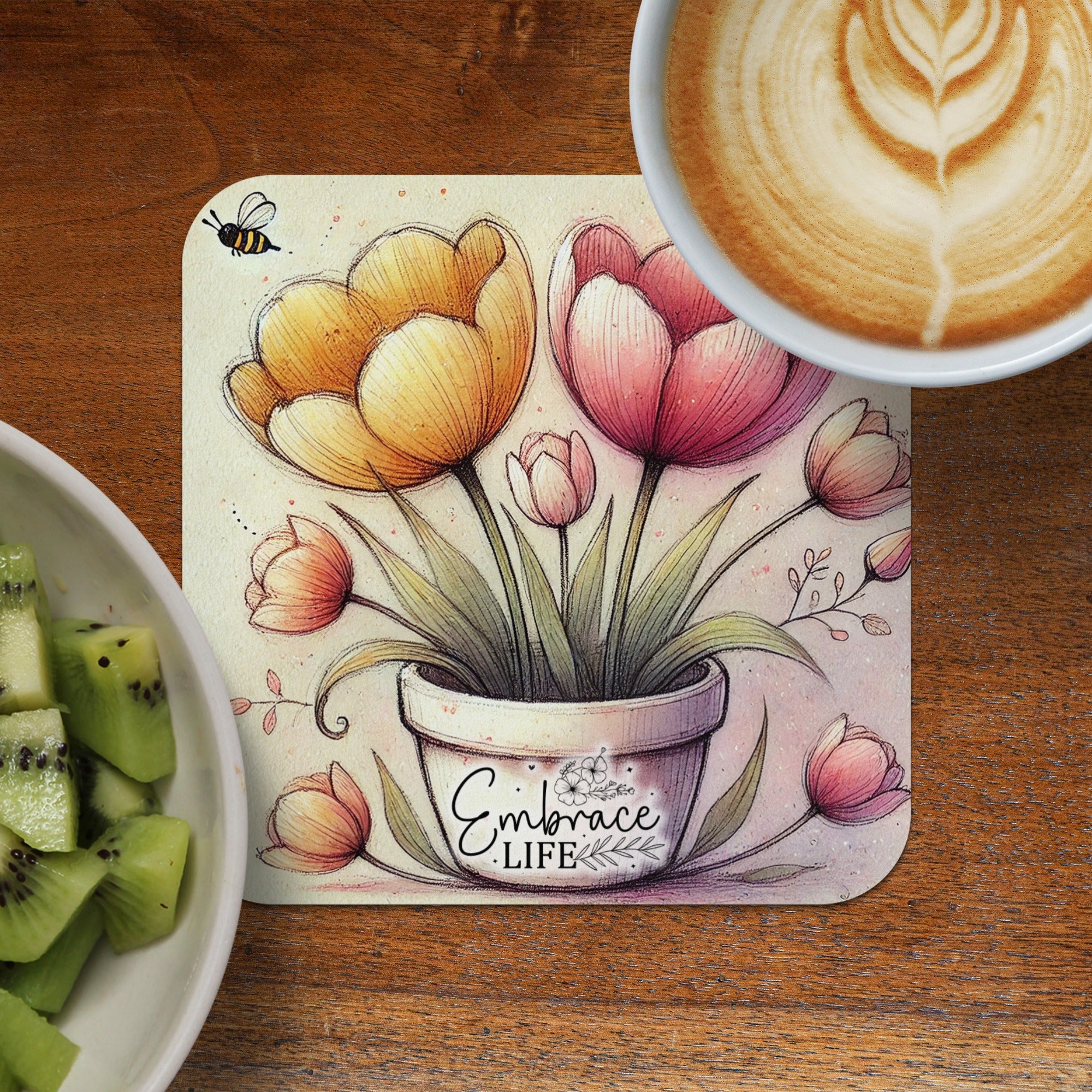 Coaster with tulips in a pot and "Embrace Life" text, next to kiwi slices and coffee.