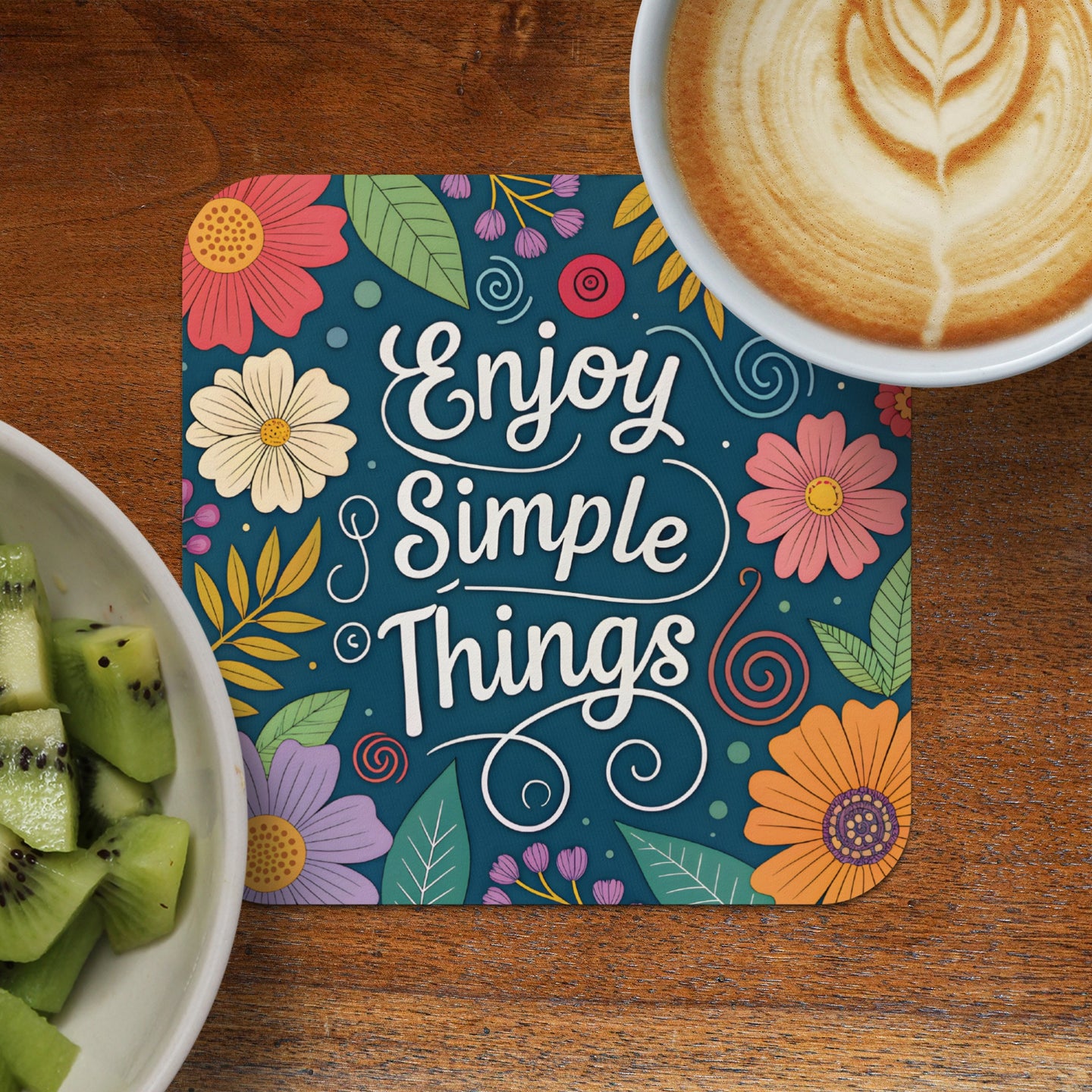 Coaster with "Enjoy Simple Things" text and floral design, next to coffee and kiwi.