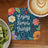 Coaster with "Enjoy Simple Things" text and floral design, next to coffee and kiwi.