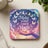 Square coaster with a hand reaching out to butterflies against a cloudy, magical sky.