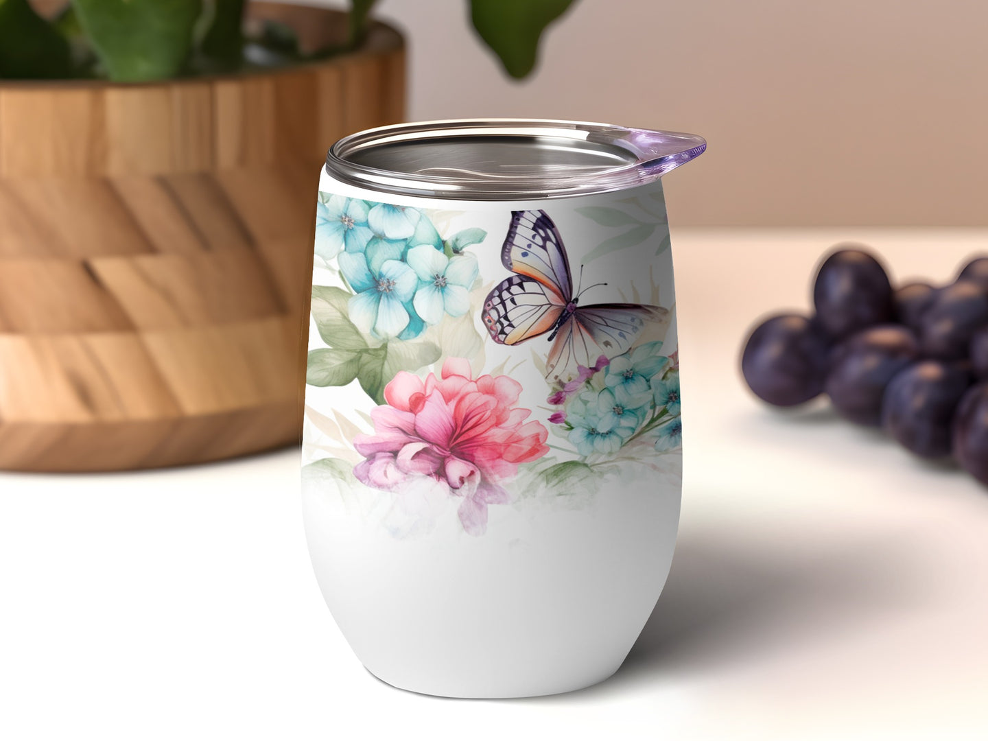 White tumbler with floral and butterfly design, against blurred background.