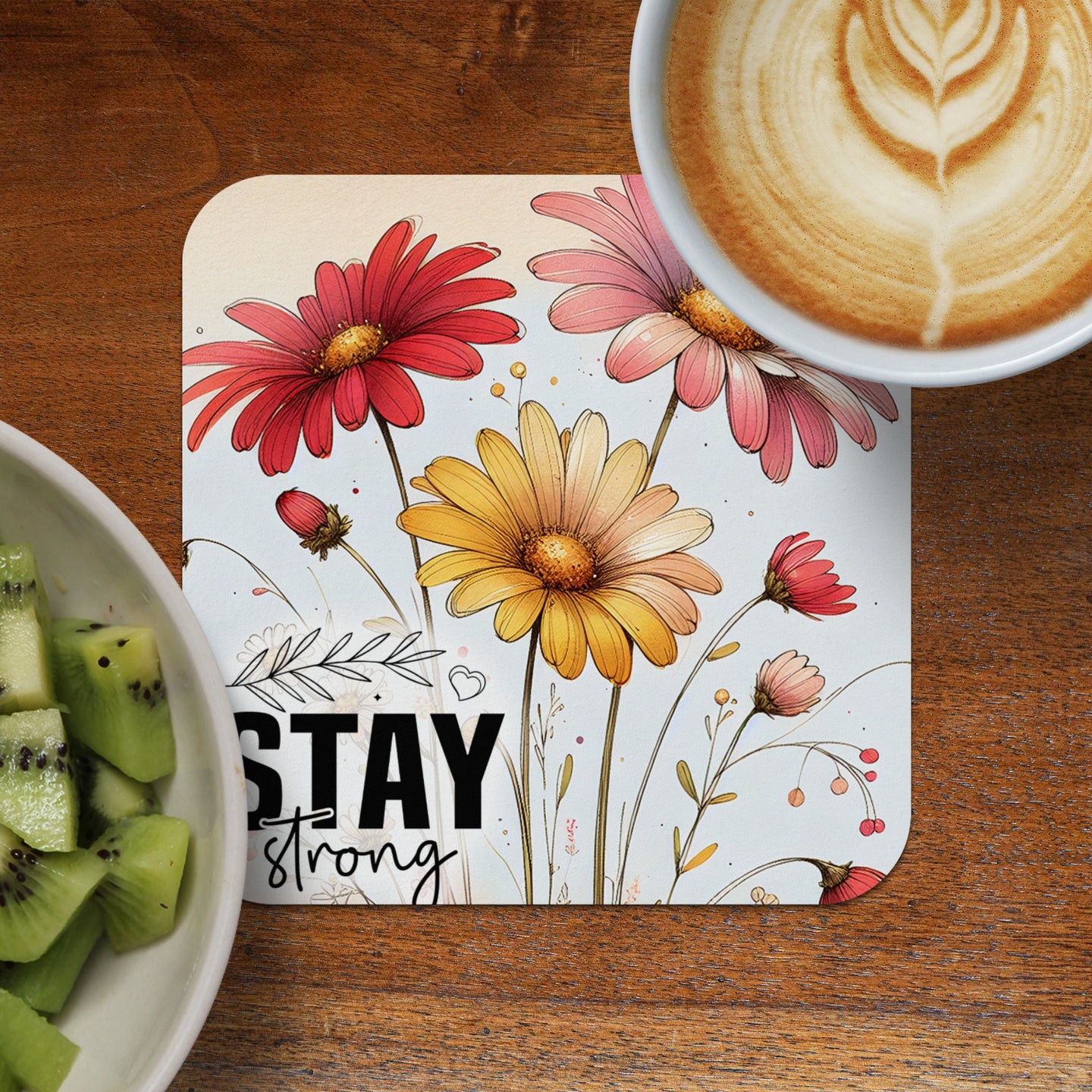 Floral coaster with "Stay strong" text next to kiwi slices and coffee.