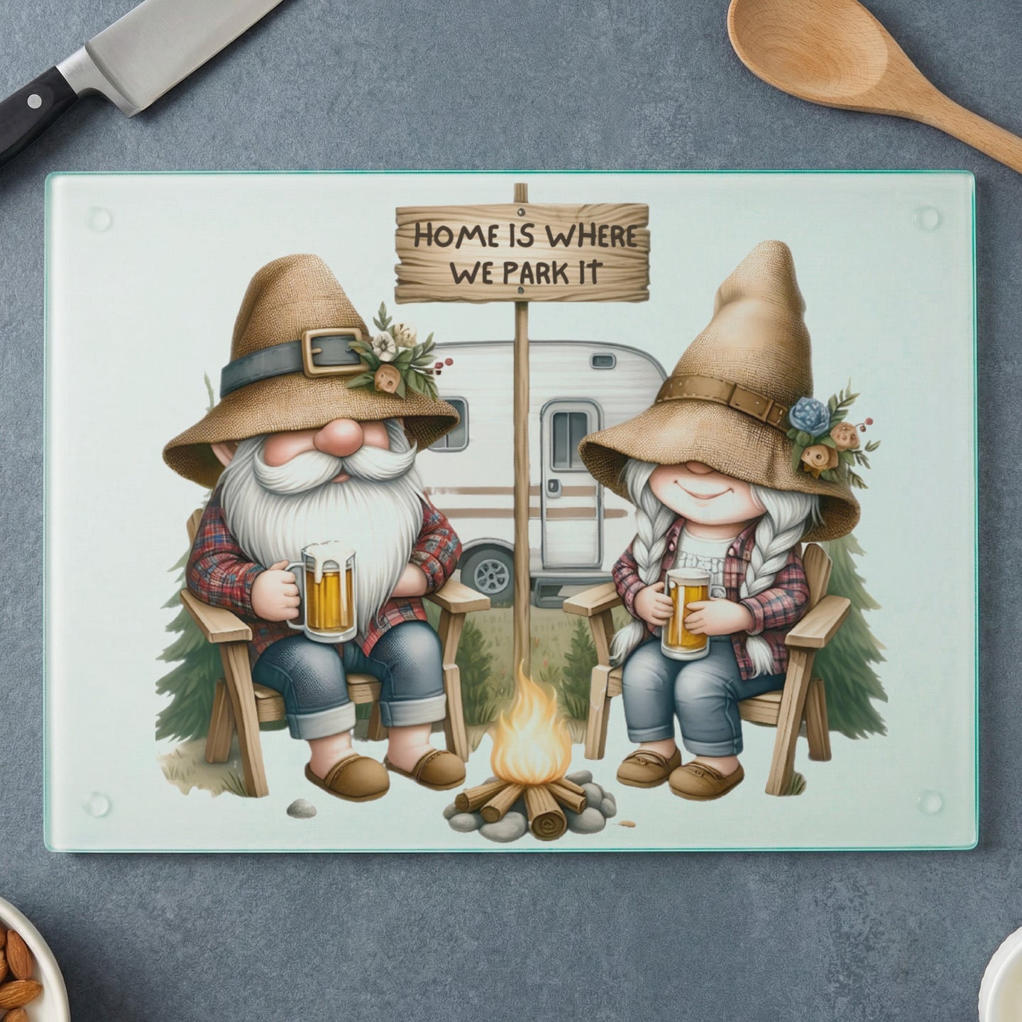 Gnomes in plaid shirts and straw hats sit by a campfire with beer, a camper behind them, and text "HOME IS WHERE WE PARK IT".
