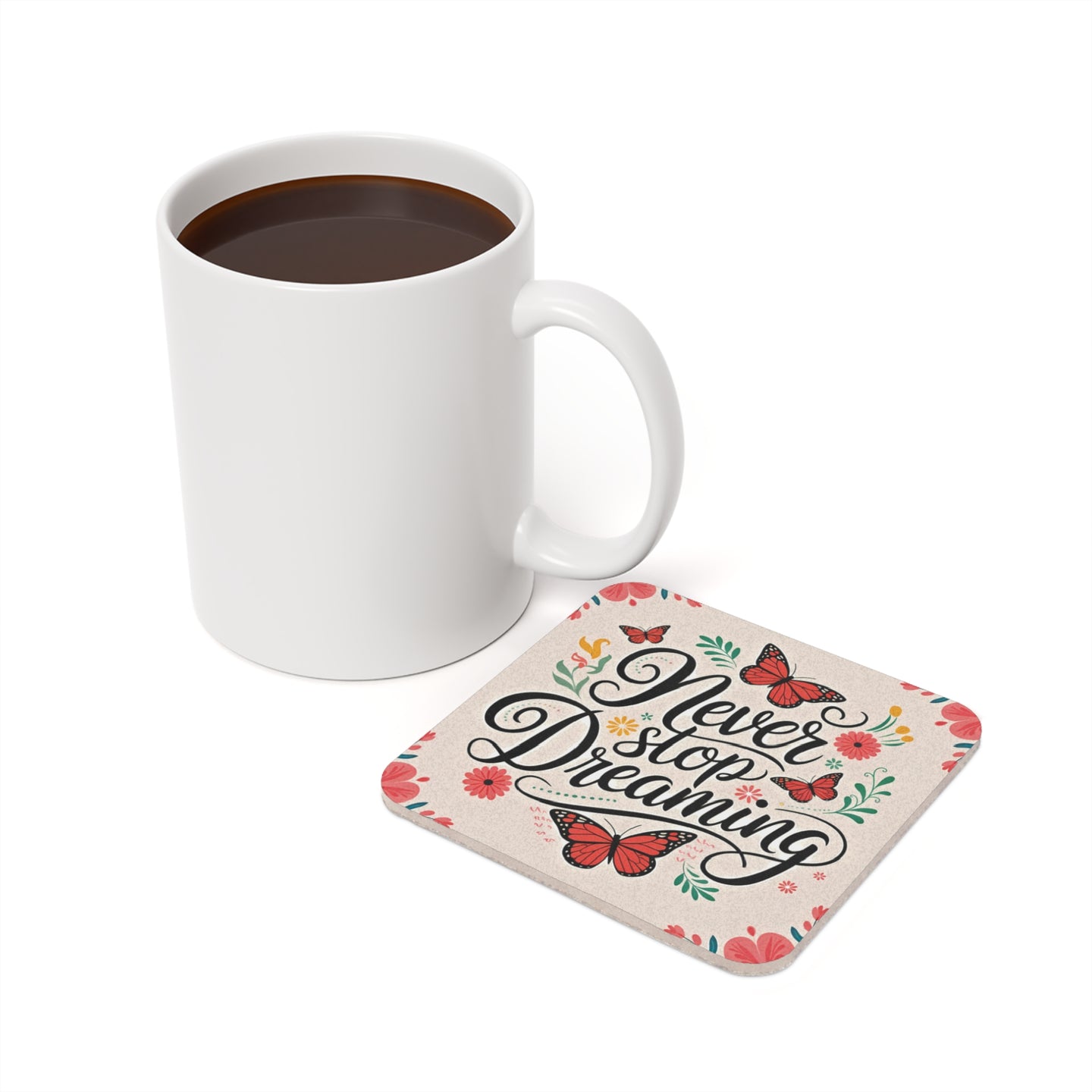 White mug next to a coaster with "Never stop dreaming" and floral butterfly design.