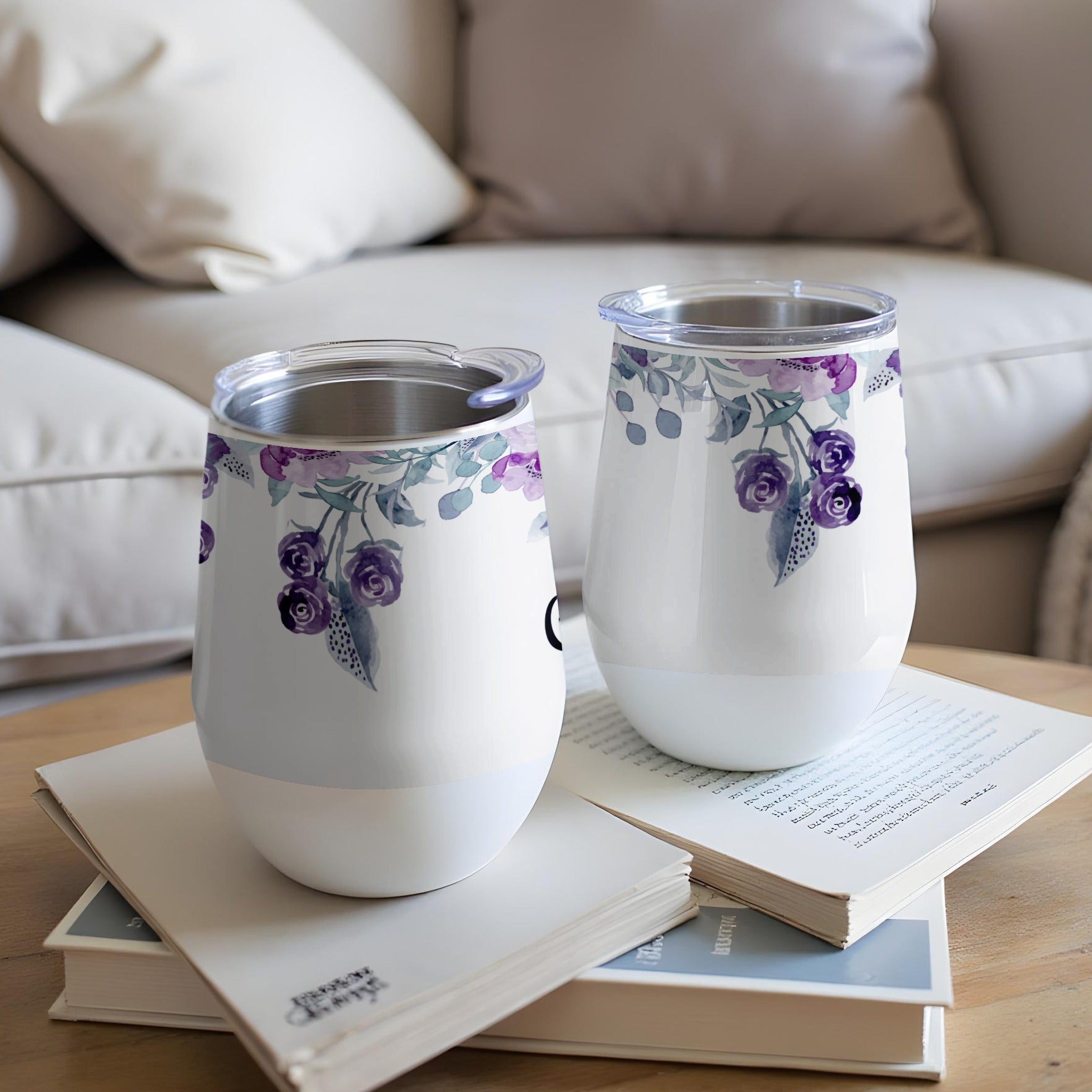 Two white floral tumblers with clear lids sit on an open book.