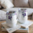 Two white floral tumblers with clear lids sit on an open book.