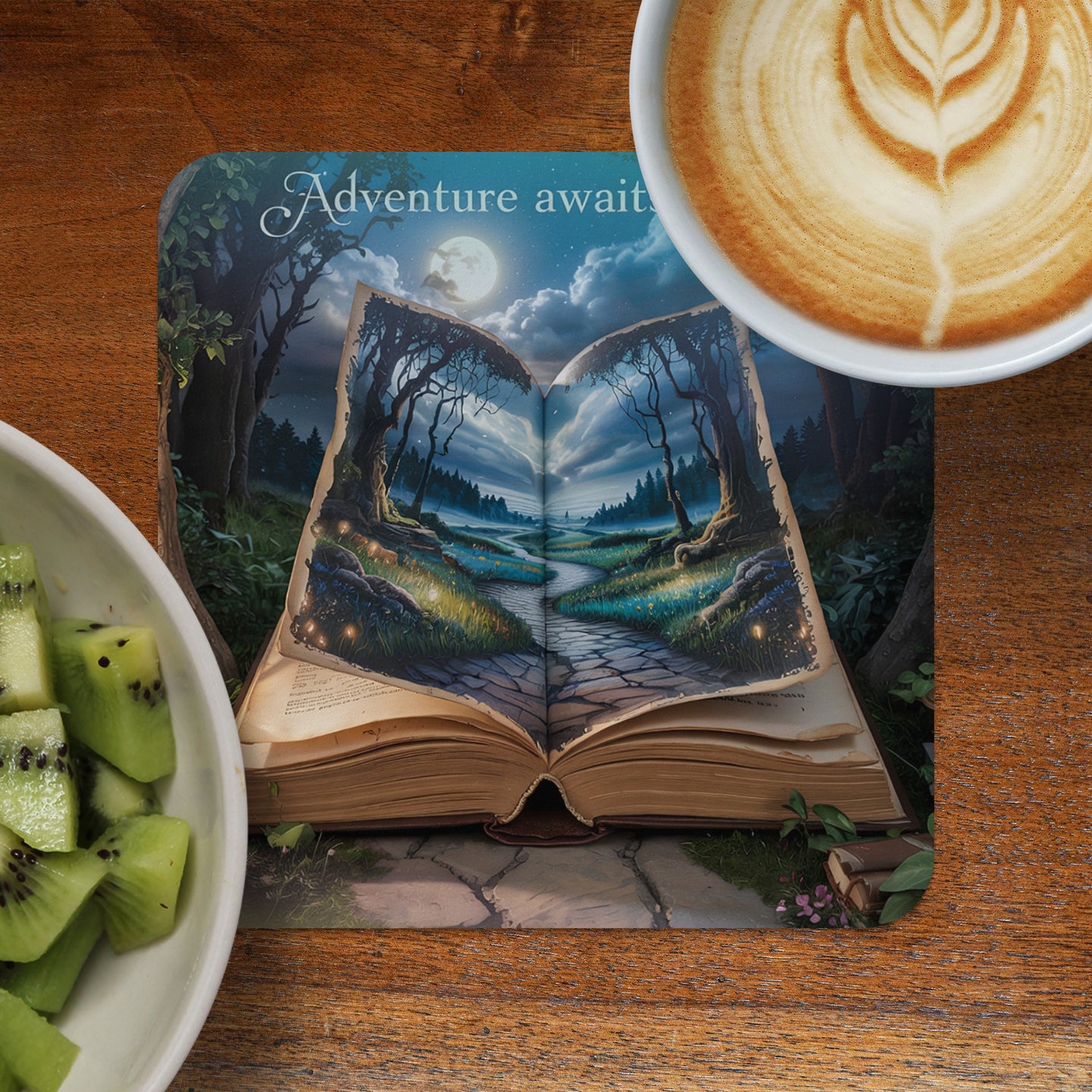 Open book with forest scene, latte art, and sliced kiwi on a wooden surface.