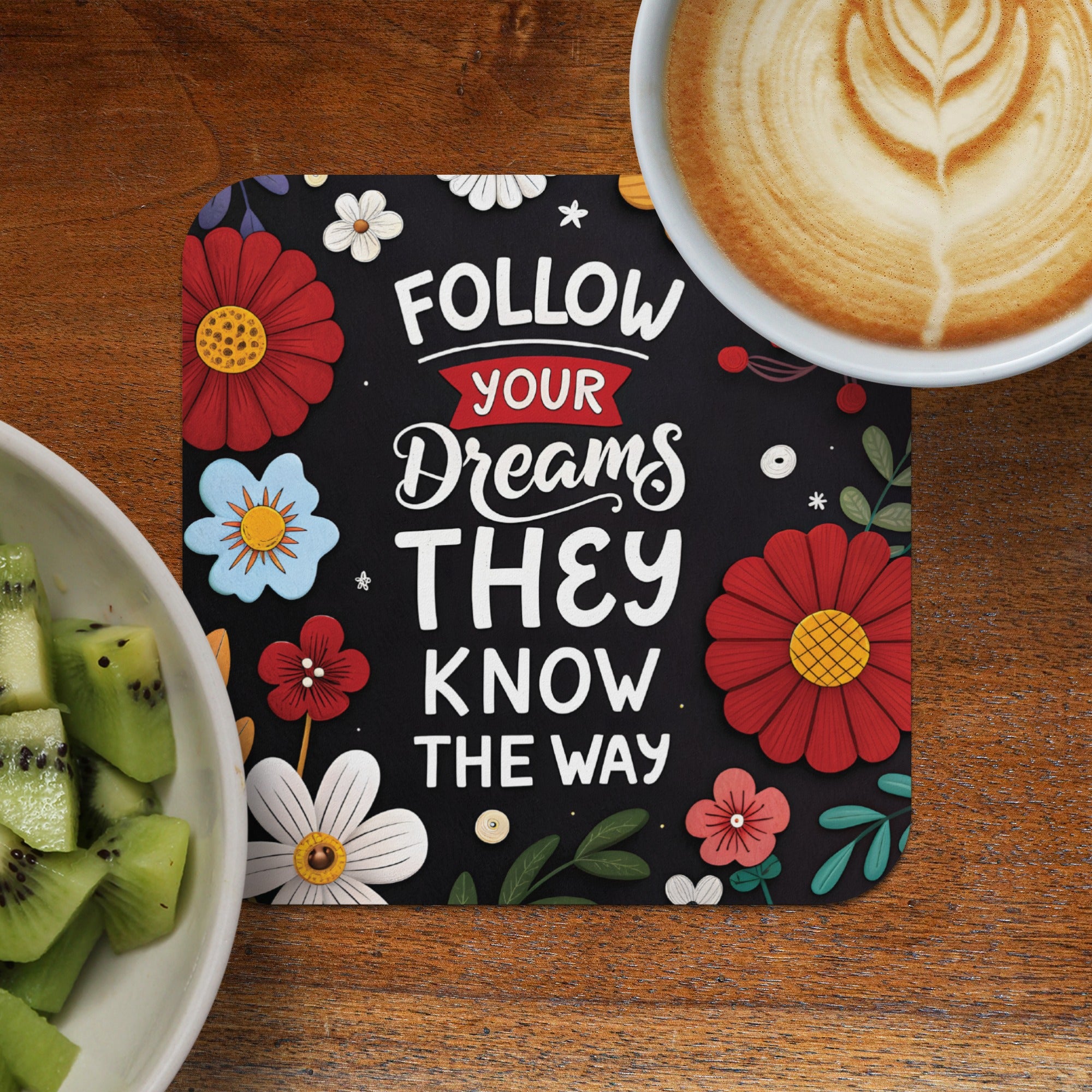 Coaster with "Follow Your Dreams" text and floral designs, next to kiwi and coffee.