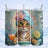 Striped cat with a towel on its head wearing a flower, holding a drink.