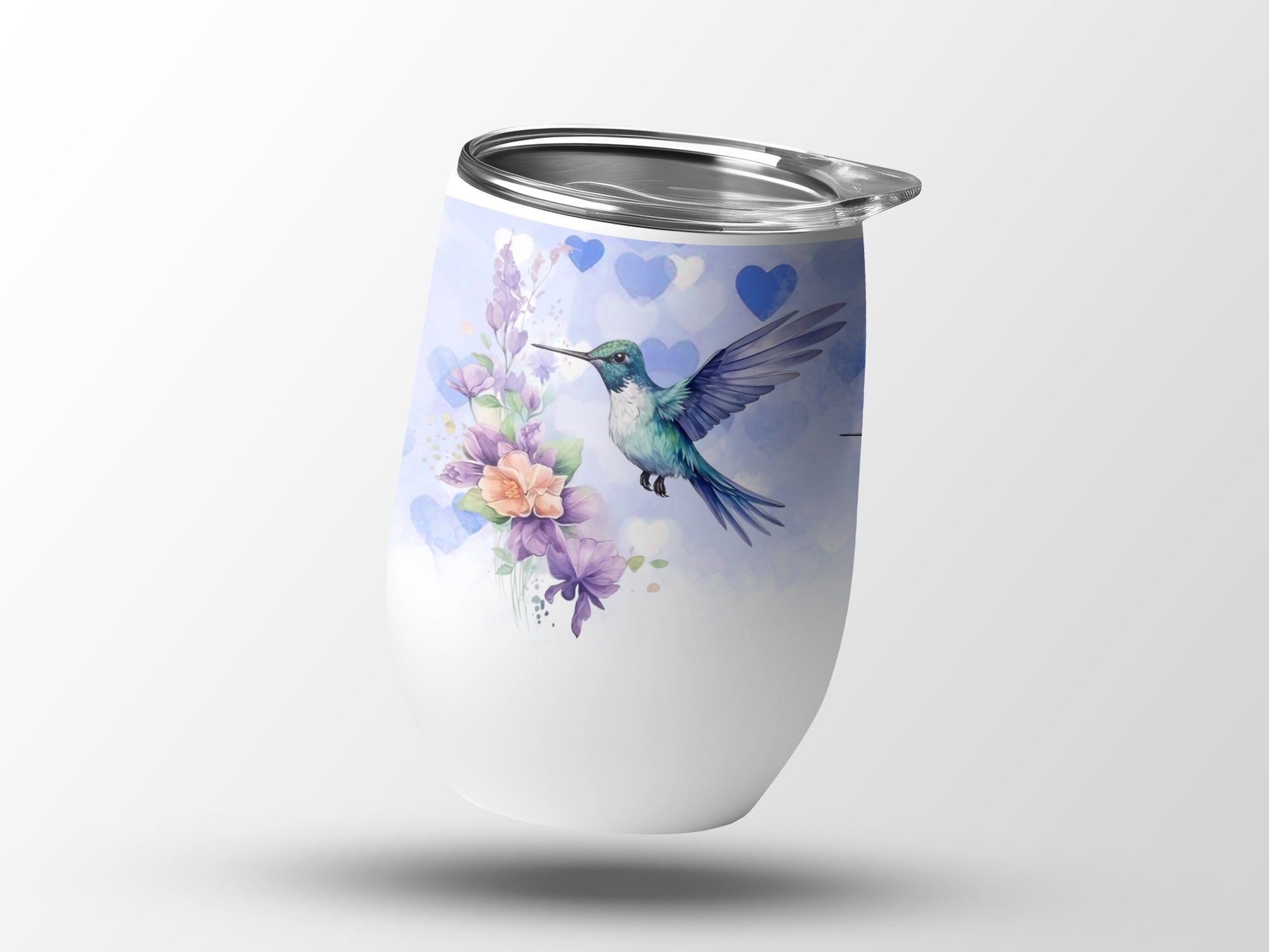 White tumbler with hummingbird and floral watercolor design, blue hearts background.