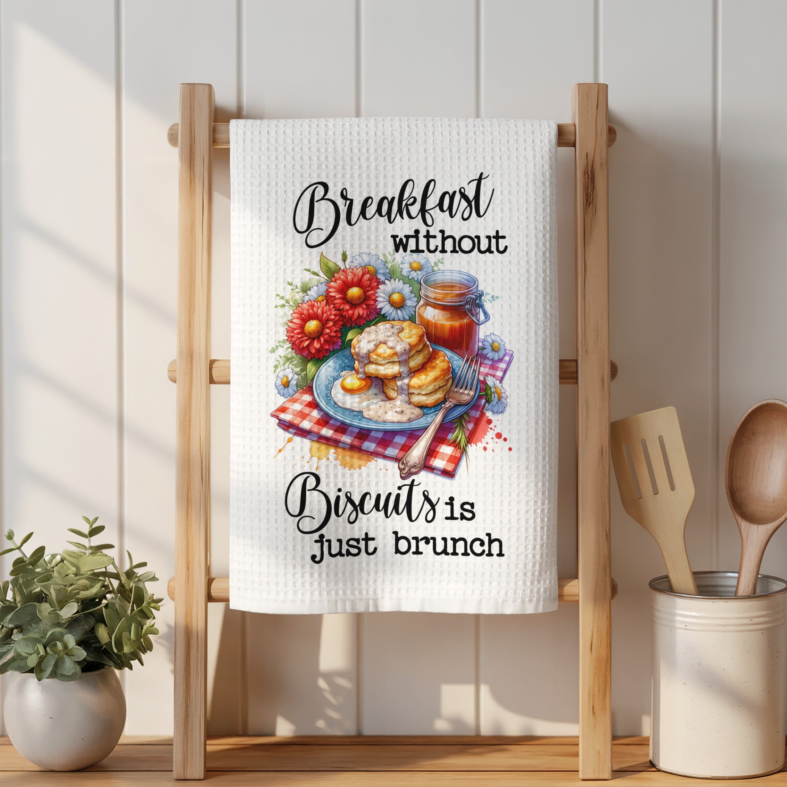 Kitchen towel with illustration of pancakes, jam, and flowers: "Breakfast without biscuits is just brunch".