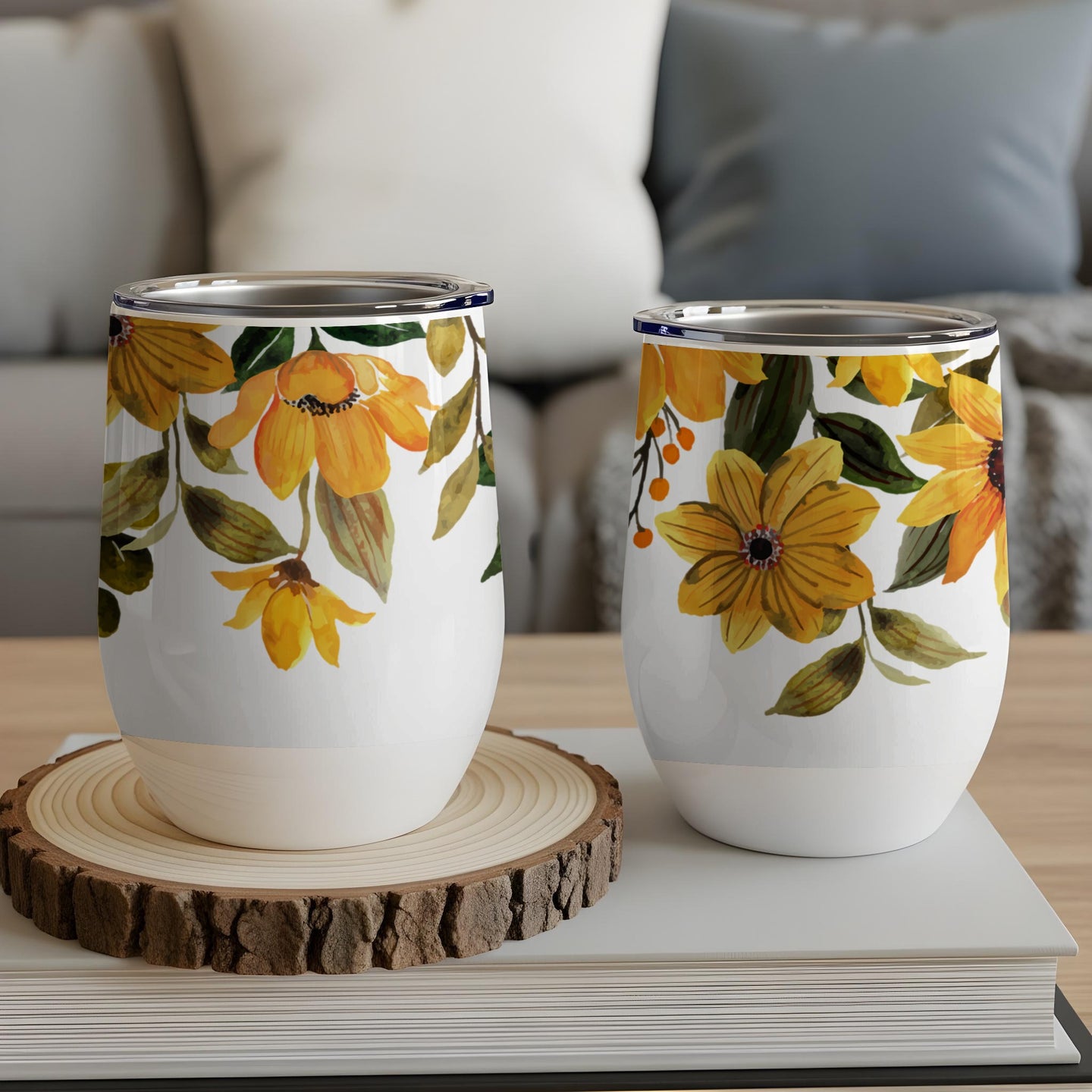 Two white tumblers with a yellow floral design, resting on a wooden coaster.