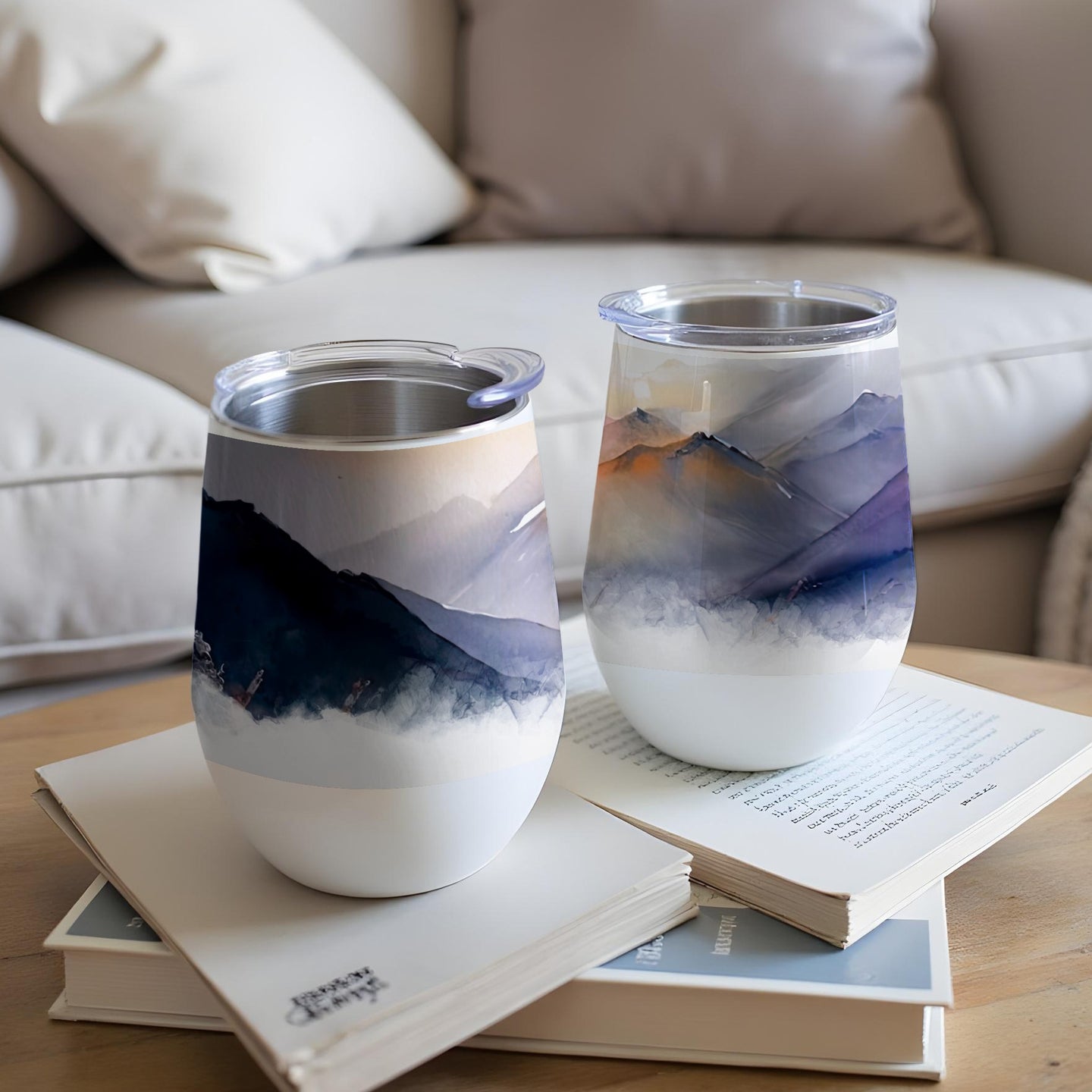 Two insulated tumblers with mountain landscape designs rest on books.