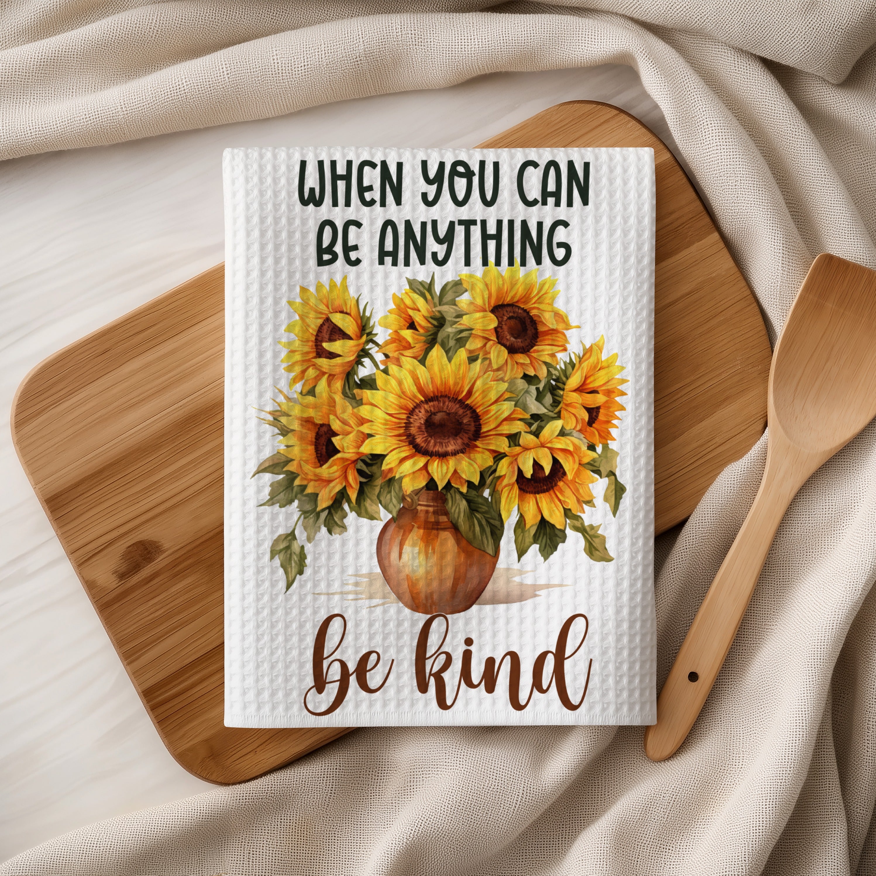Text reads: When you can be anything, be kind. Sunflowers in vase on white waffle towel.