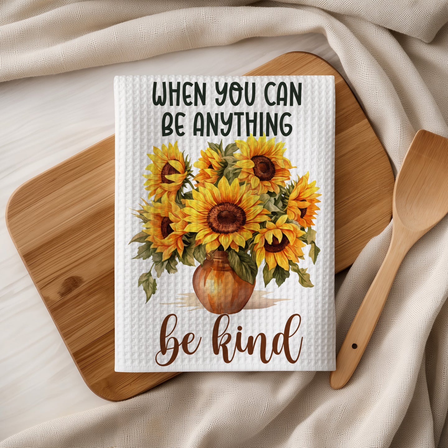 Text reads: When you can be anything, be kind. Sunflowers in vase on white waffle towel.