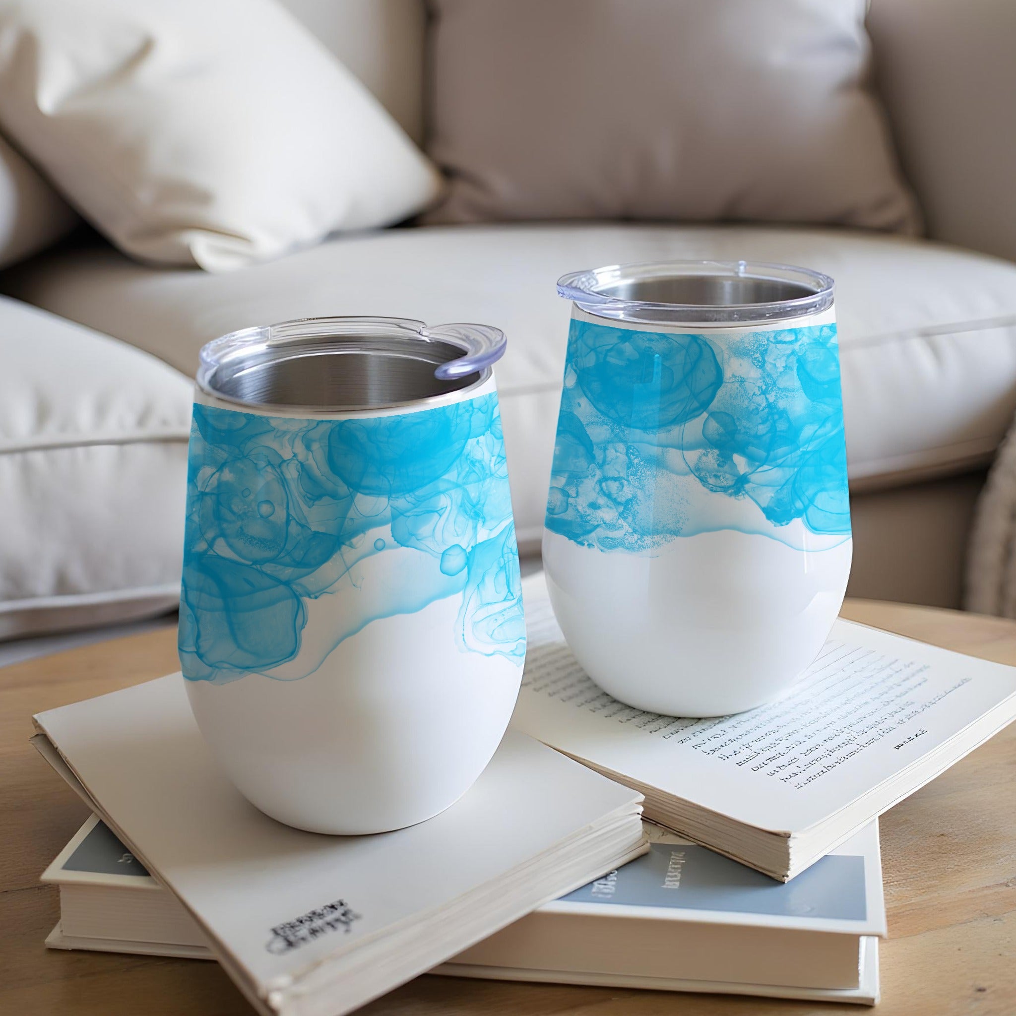 Two white tumblers with blue watercolor designs sit on books.